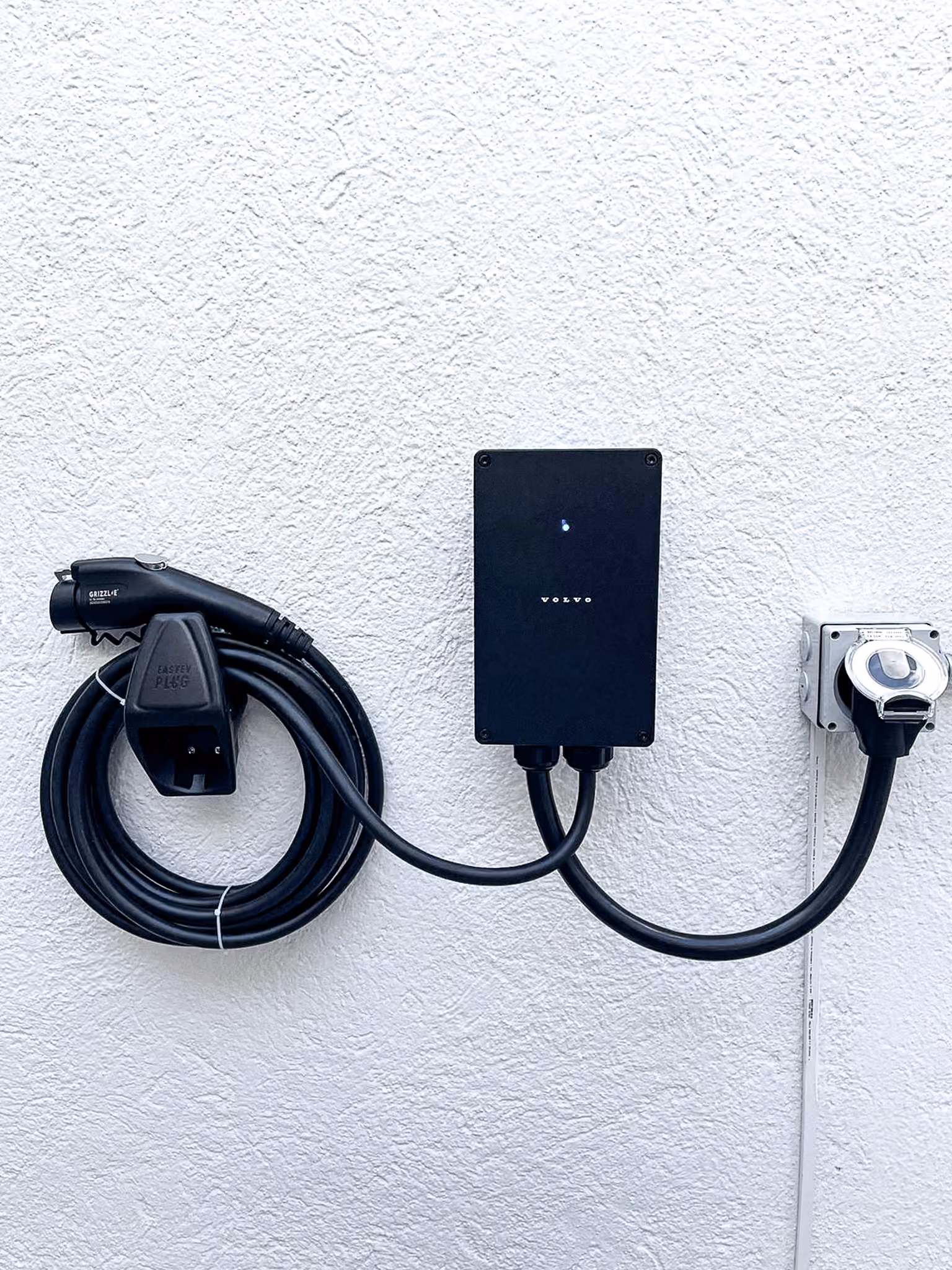 Cargador de pared Volvo en muro blanco, con contacto dedicado y cable montado al lado.